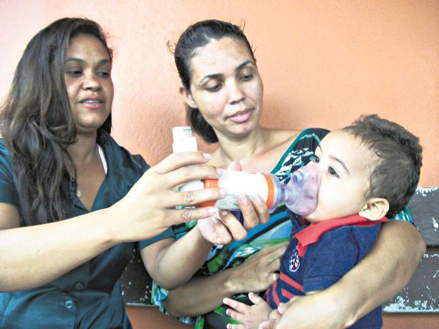 A mãe Kelly Pereira e a tia Keila seguram o pequeno Miguel para aplicar bombinha por conta de bronquite asmática. Foto: Bruno Lyra